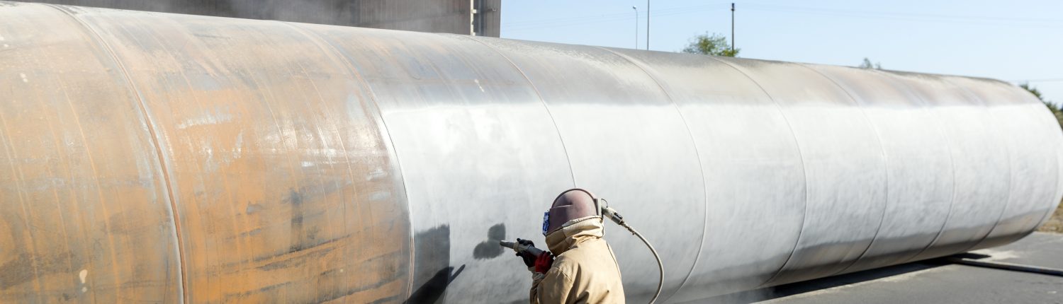 View of the manuel sandblasting to the large pipe. Abrasive blasting more commonly known as sandblasting is the operation of forcibly propelling a stream of abrasive material against a surface under high pressure.